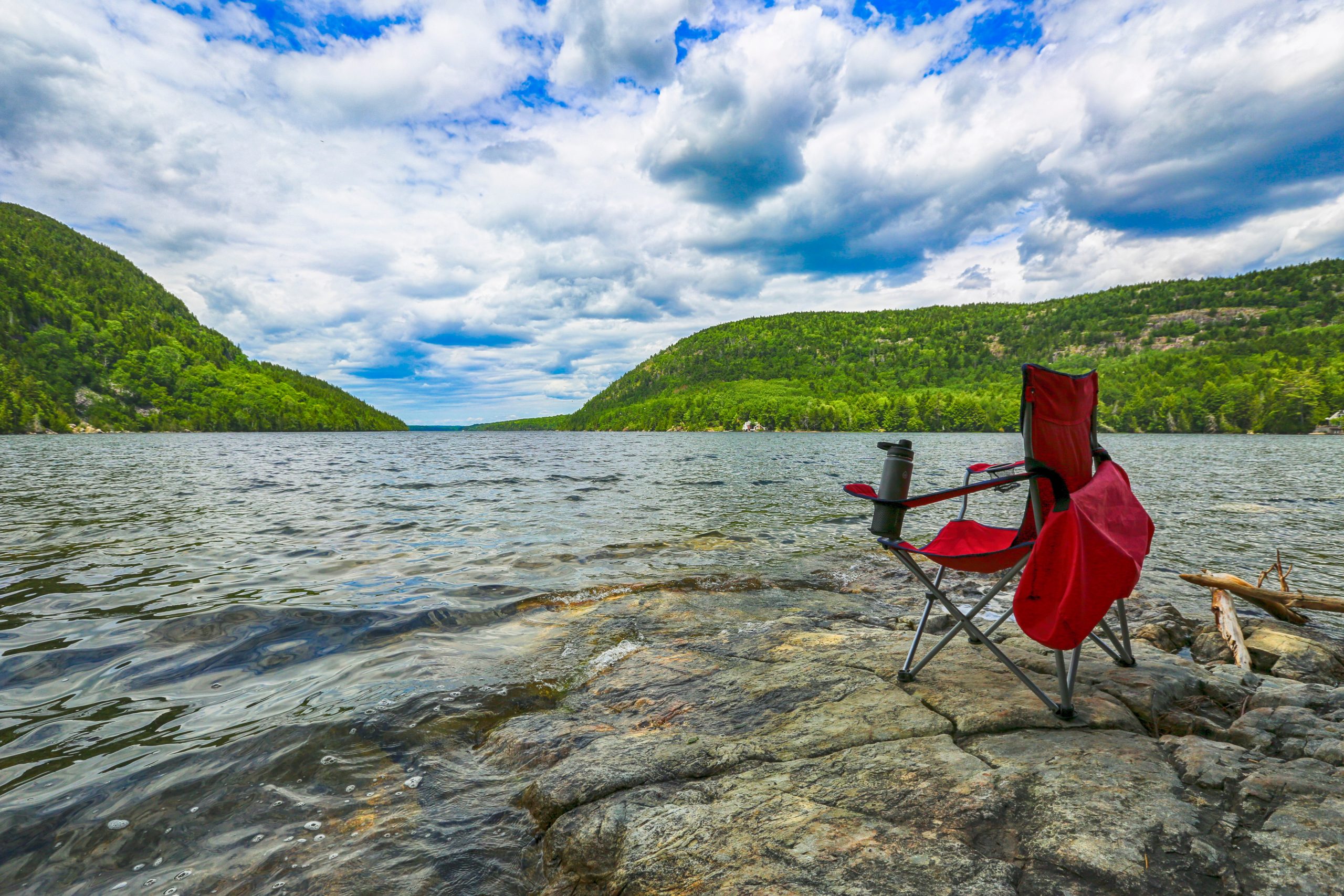 Camping chair on a rock facing a body of water.